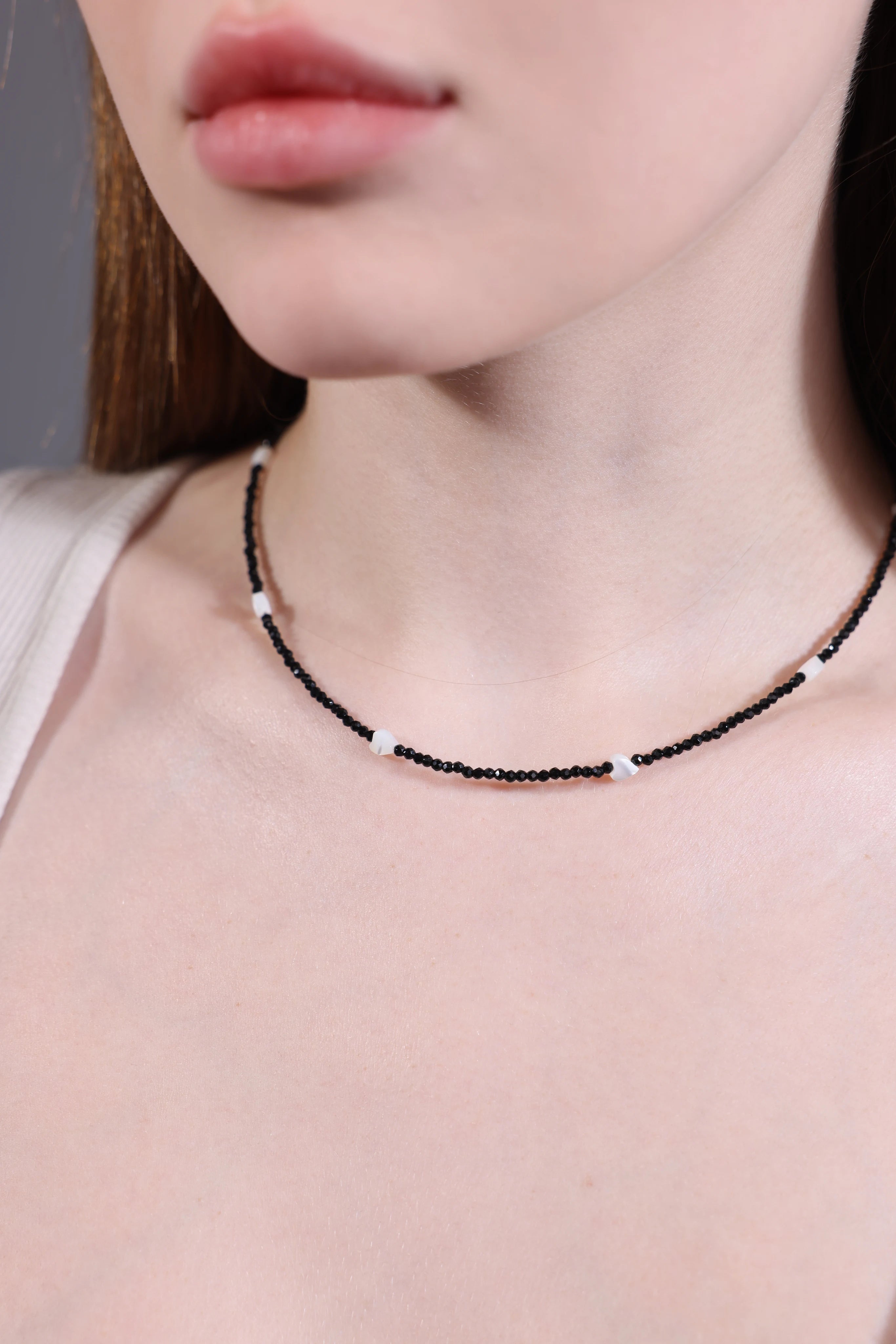 close-up of model wearing black seed bead choker with white shell heart beads